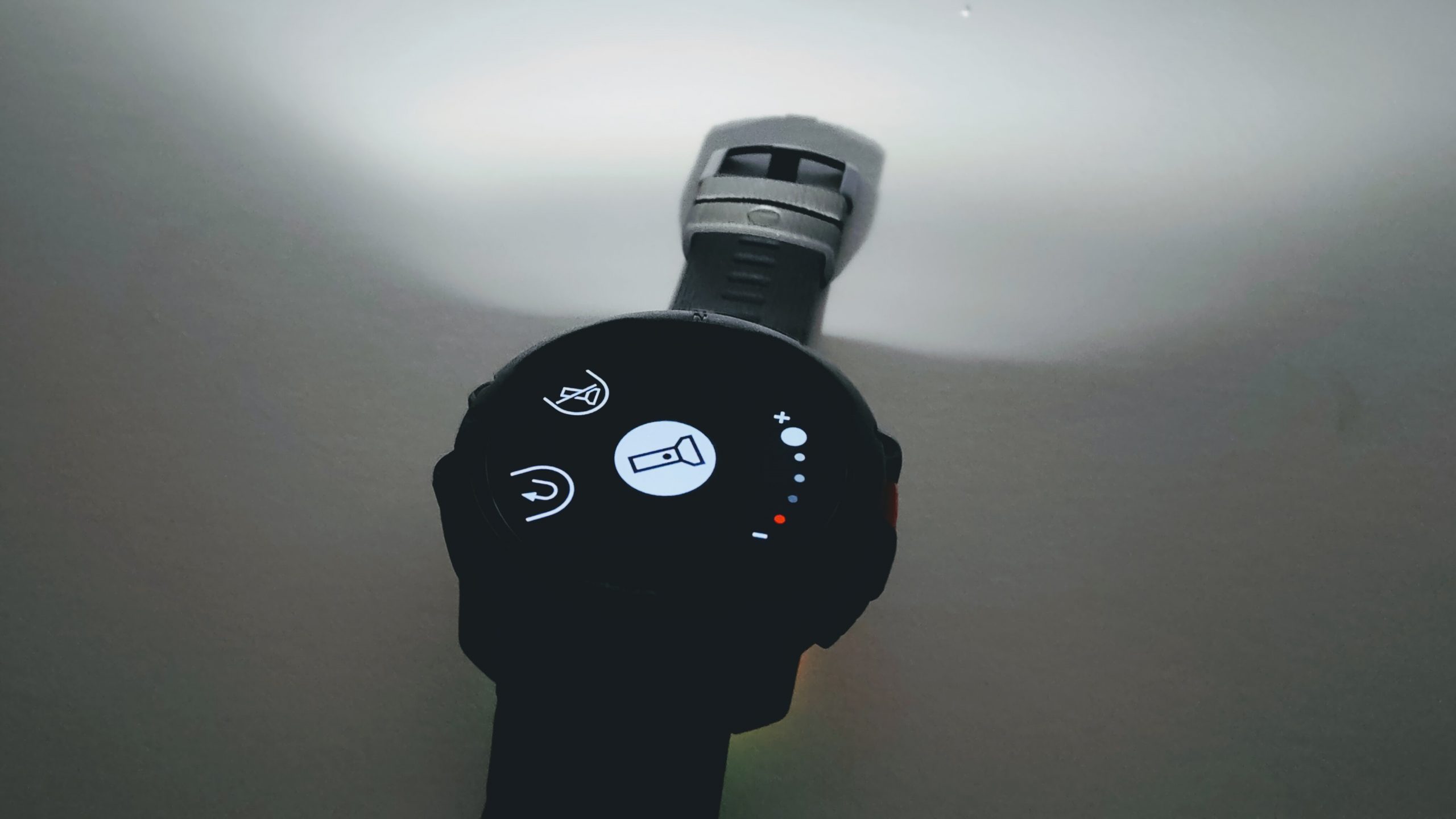 Close-up of a circular smartwatch on a dark strap, displaying icons including microphone, mute, and power on a black screen.