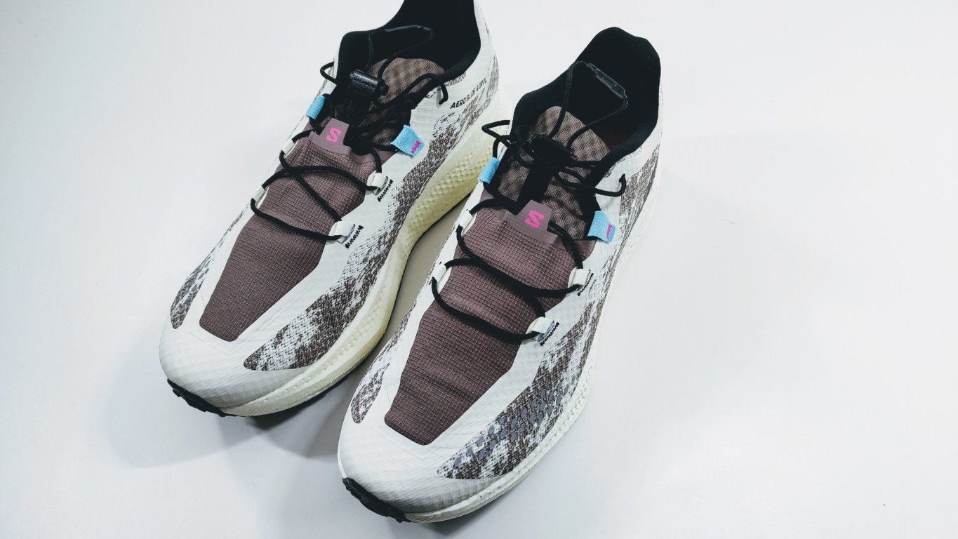 Pair of gray and white running shoes with black laces, blue lace loops, and pink S logos on a light surface.