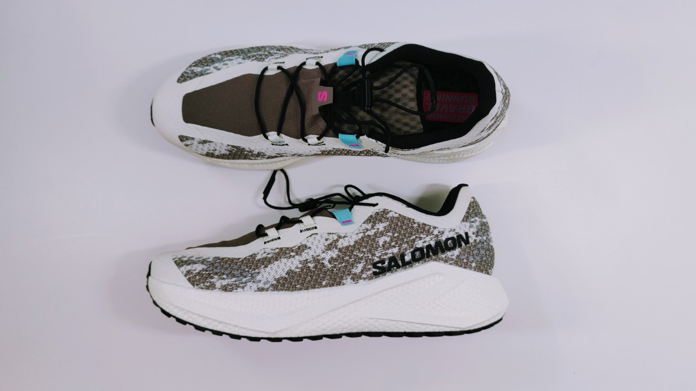 Pair of Salomon running shoes on a light background, featuring white midsoles and gray camo-pattern uppers.