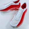 Pair of white and red running shoes with white laces, angled on a white surface, showing red side panels and subtle stripes.
