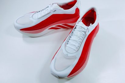 Pair of white and red running shoes with white laces, angled on a white surface, showing red side panels and subtle stripes.