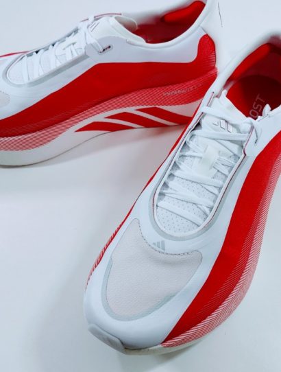 Pair of white and red running shoes with white laces, angled on a white surface, showing red side panels and subtle stripes.