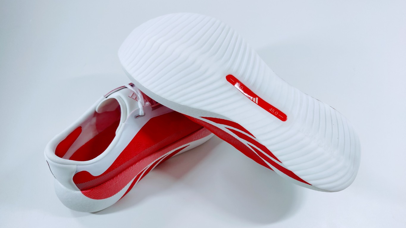 White athletic shoe with red lining and diagonal red stripes, showing the thick ridged sole.