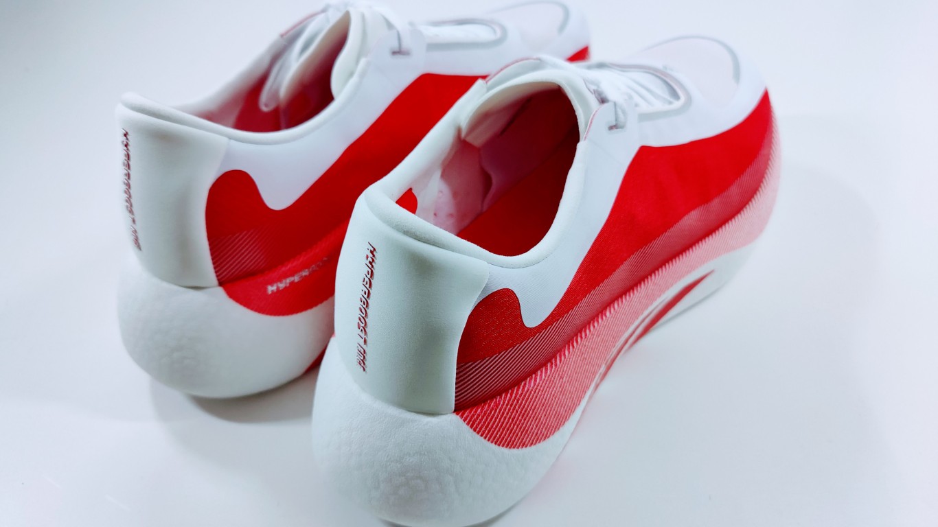 Pair of white and red athletic sneakers photographed from the rear, resting on a white surface.