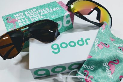 Sunglasses with tortoiseshell frame and mirrored lenses on a white surface beside a teal Goodr box and a patterned drawstring pouch.