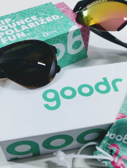 Sunglasses with tortoiseshell frame and mirrored lenses on a white surface beside a teal Goodr box and a patterned drawstring pouch.