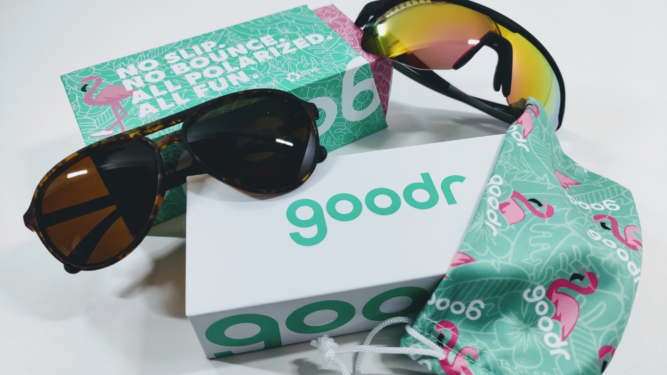 Sunglasses with tortoiseshell frame and mirrored lenses on a white surface beside a teal Goodr box and a patterned drawstring pouch.