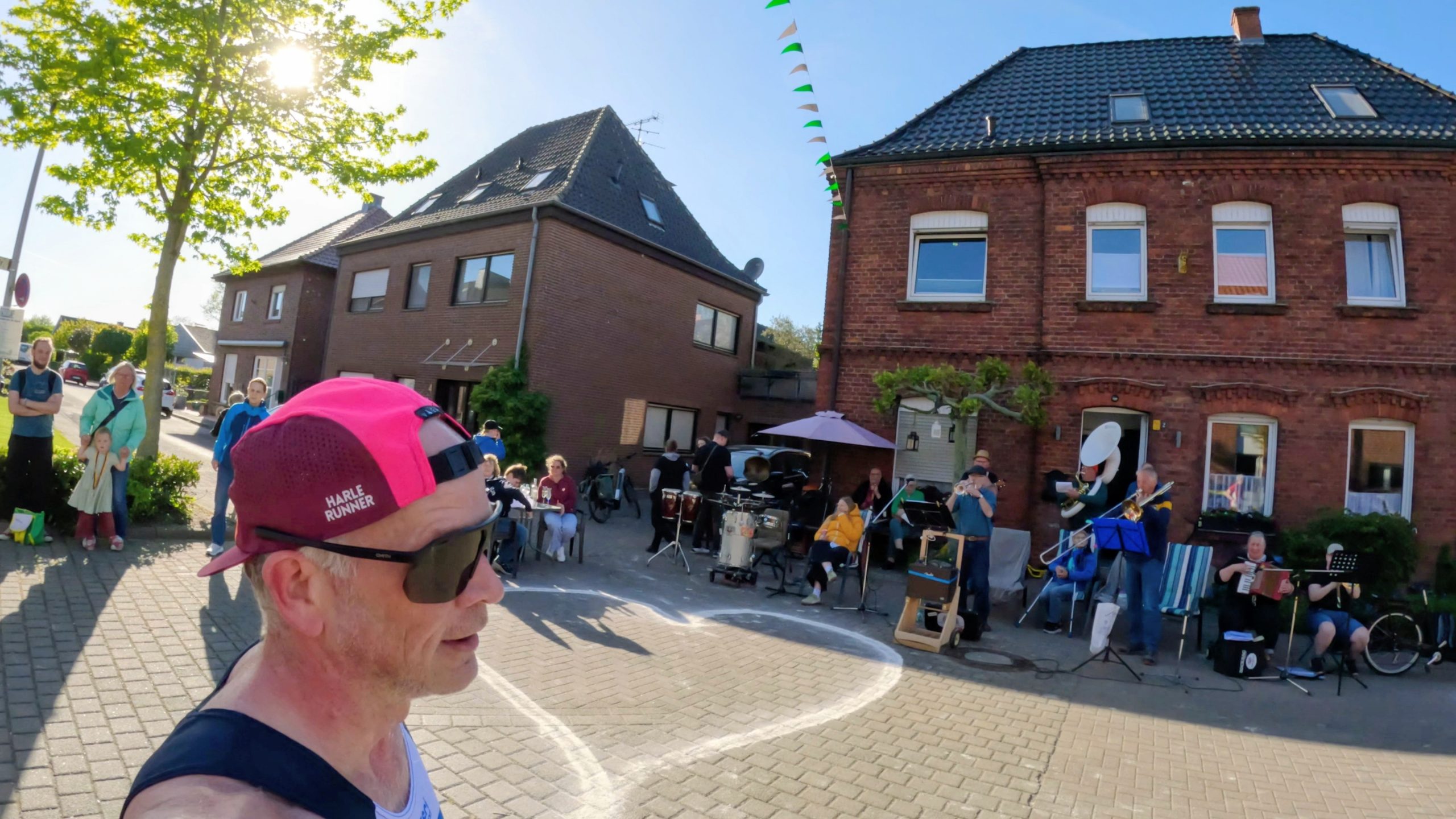 Group of people watching a street band perform outside brick houses on a sunny day.