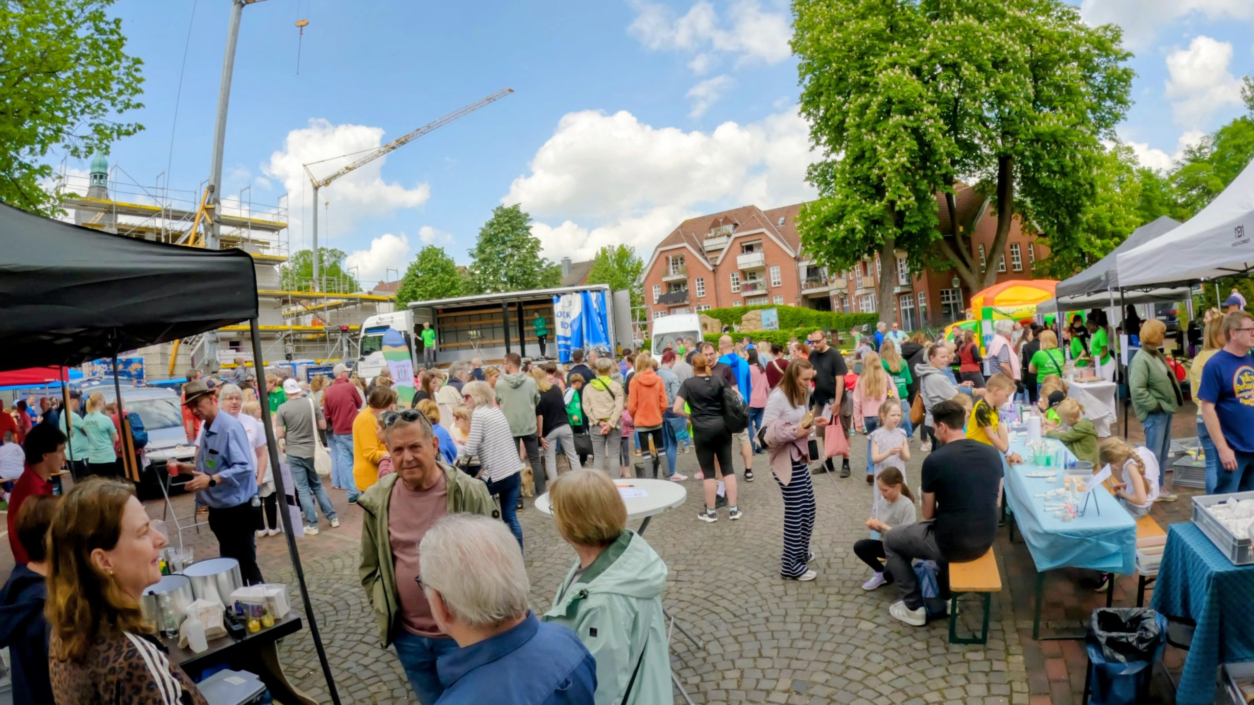 Crowded outdoor street fair with stalls, tents, and people browsing on a sunny day.