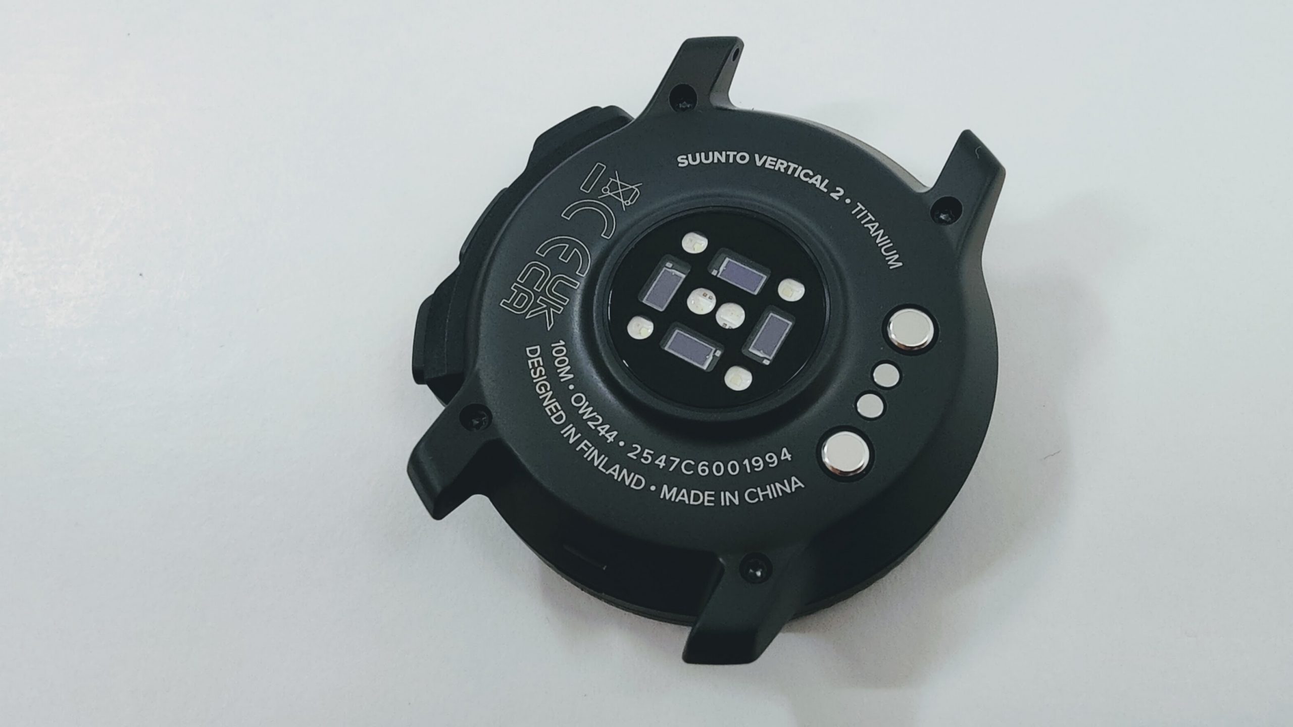 Close-up of the back of a Suunto Vertical 2 Titanium sports watch, showing the circular sensor array and branding on a light surface.