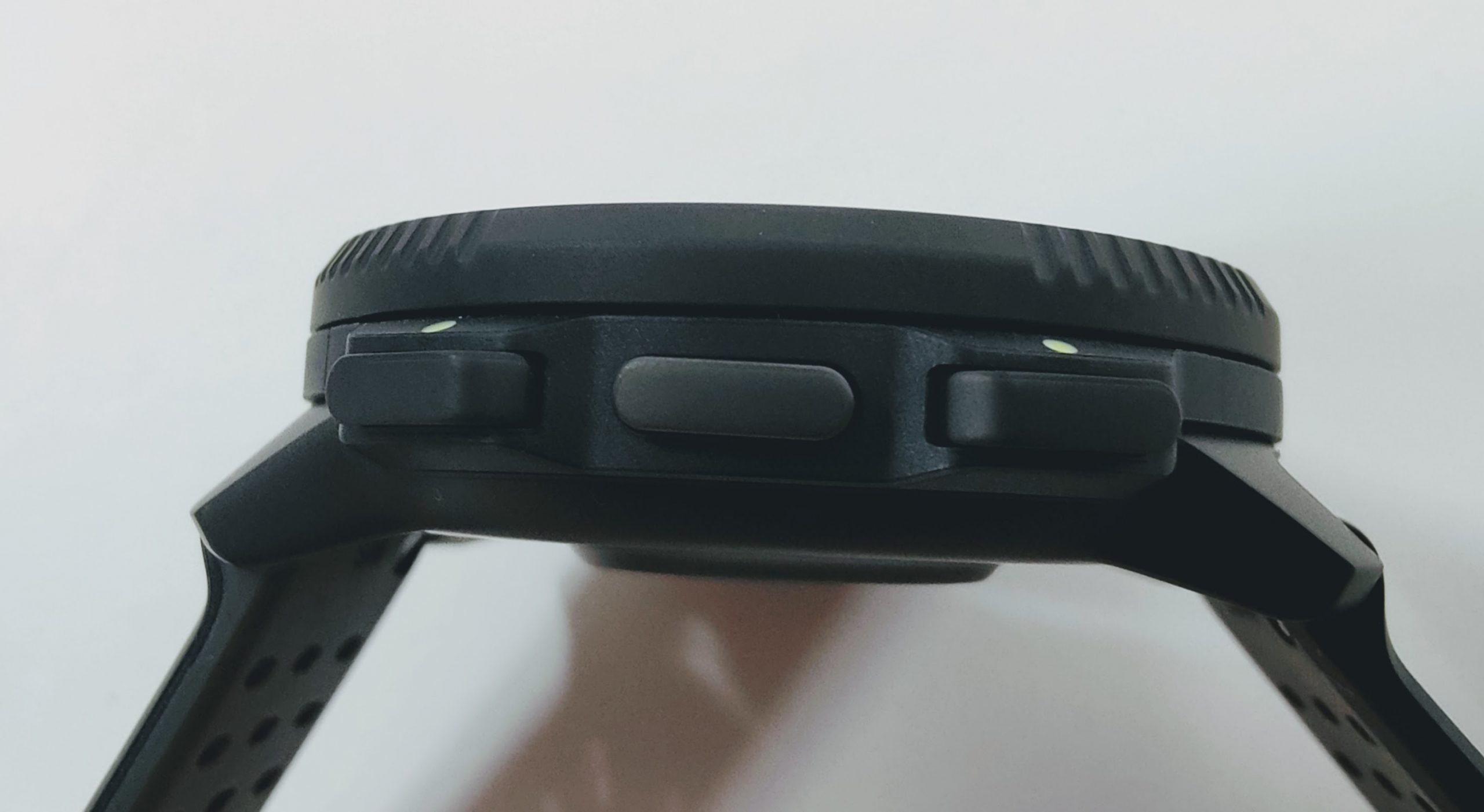 Close-up of a black wearable device with a ridged, circular top (crown) and two side push-buttons.