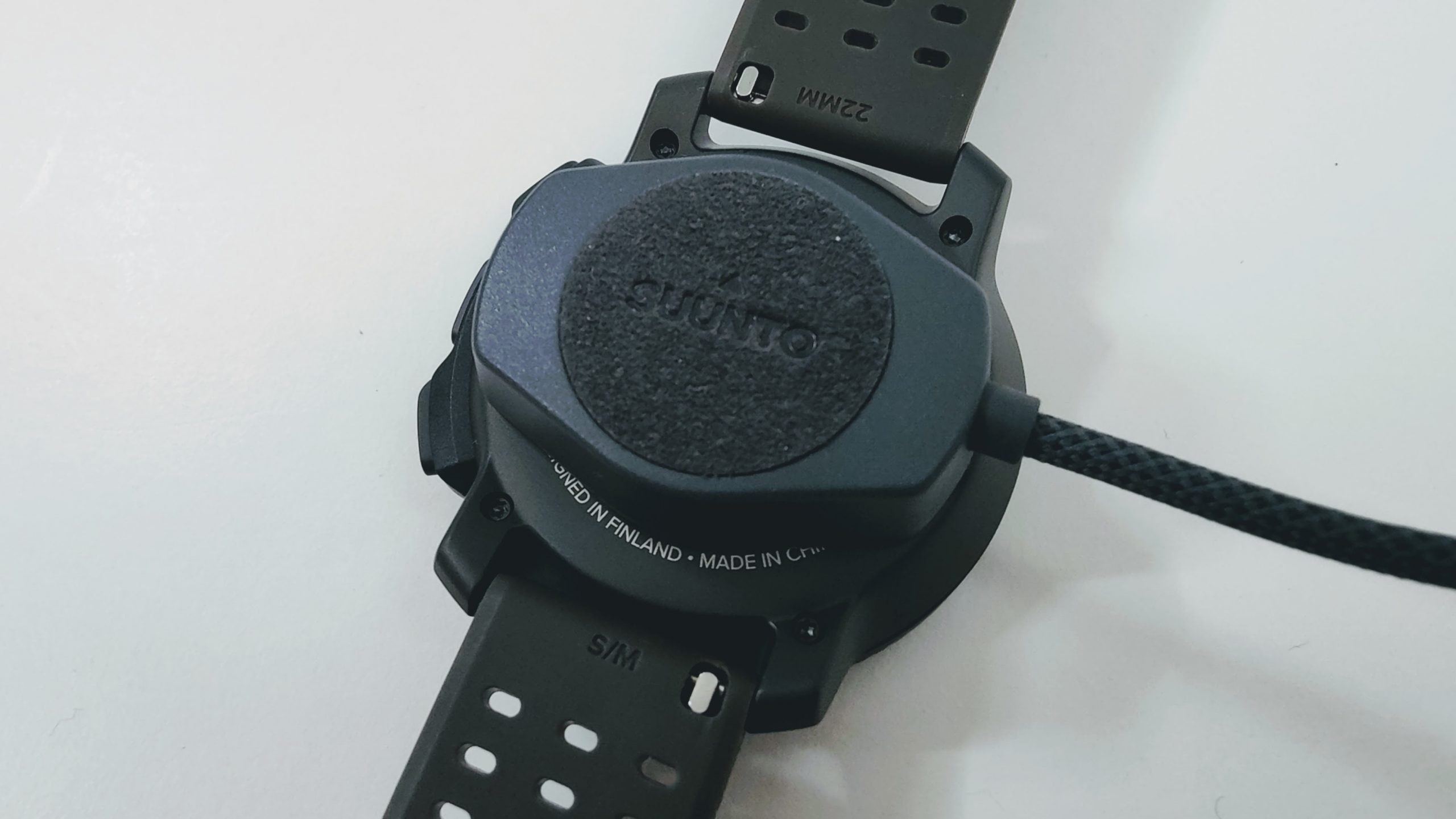 Back view of a Suunto sports watch with a black perforated strap; the circular back plate shows the Suunto logo and 'MADE IN FINLAND' inscription.