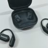 Wireless black earbuds with charging case open; Suunto logo on earbuds, one earbud outside case and one nearby on a light surface.