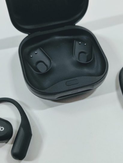 Wireless black earbuds with charging case open; Suunto logo on earbuds, one earbud outside case and one nearby on a light surface.