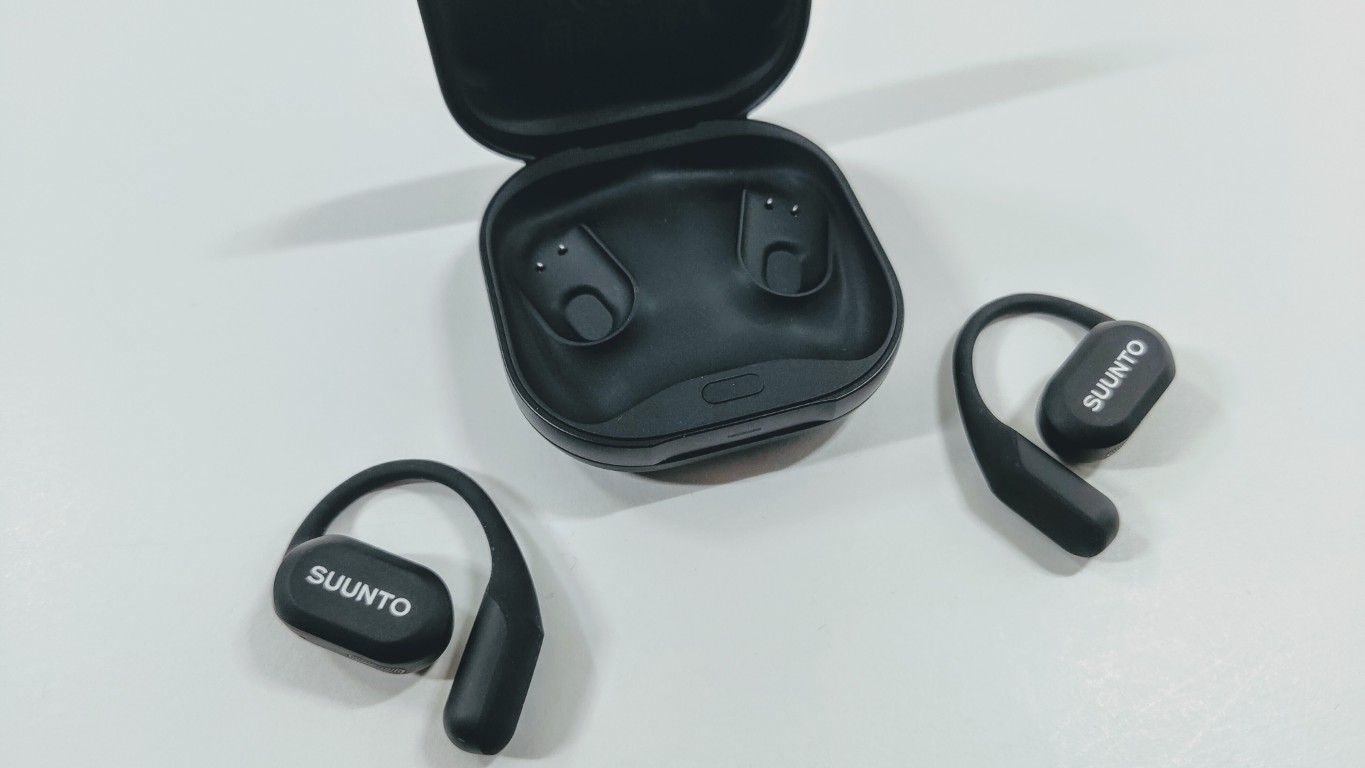 Wireless black earbuds with charging case open; Suunto logo on earbuds, one earbud outside case and one nearby on a light surface.