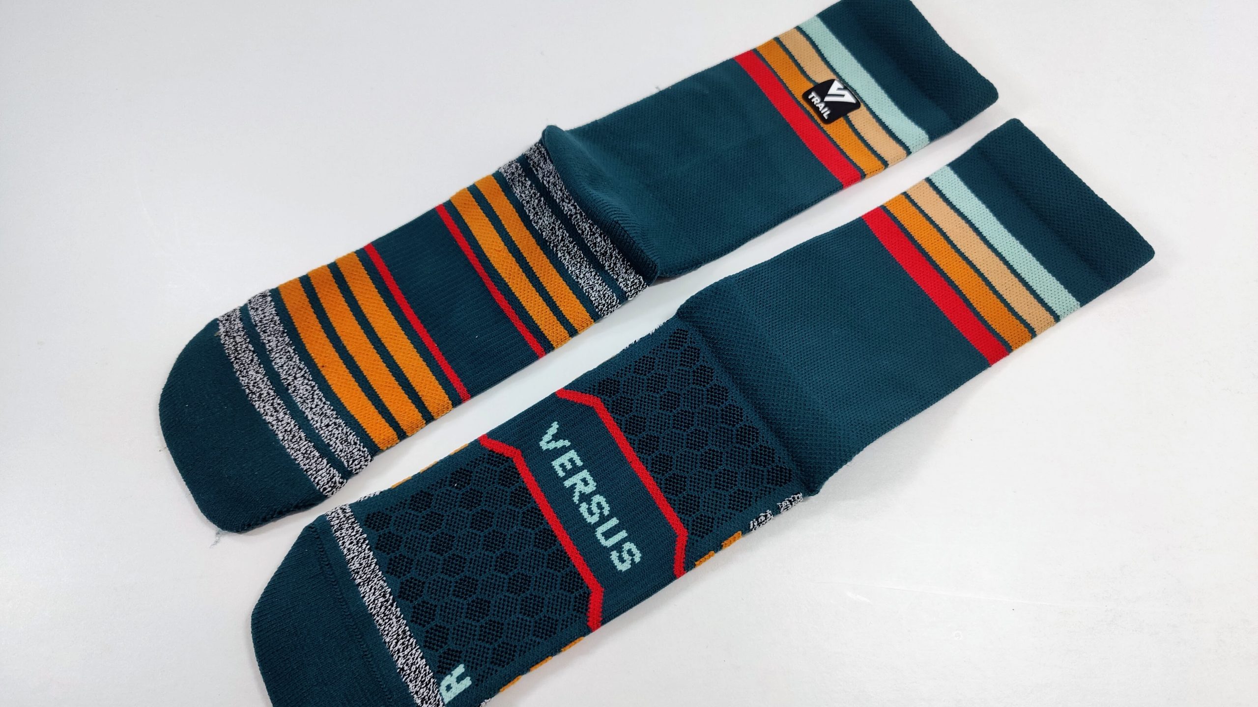 Teal athletic socks with orange, red, beige and light blue stripes and a small black logo tag on the upper leg area, laid flat on a white surface.