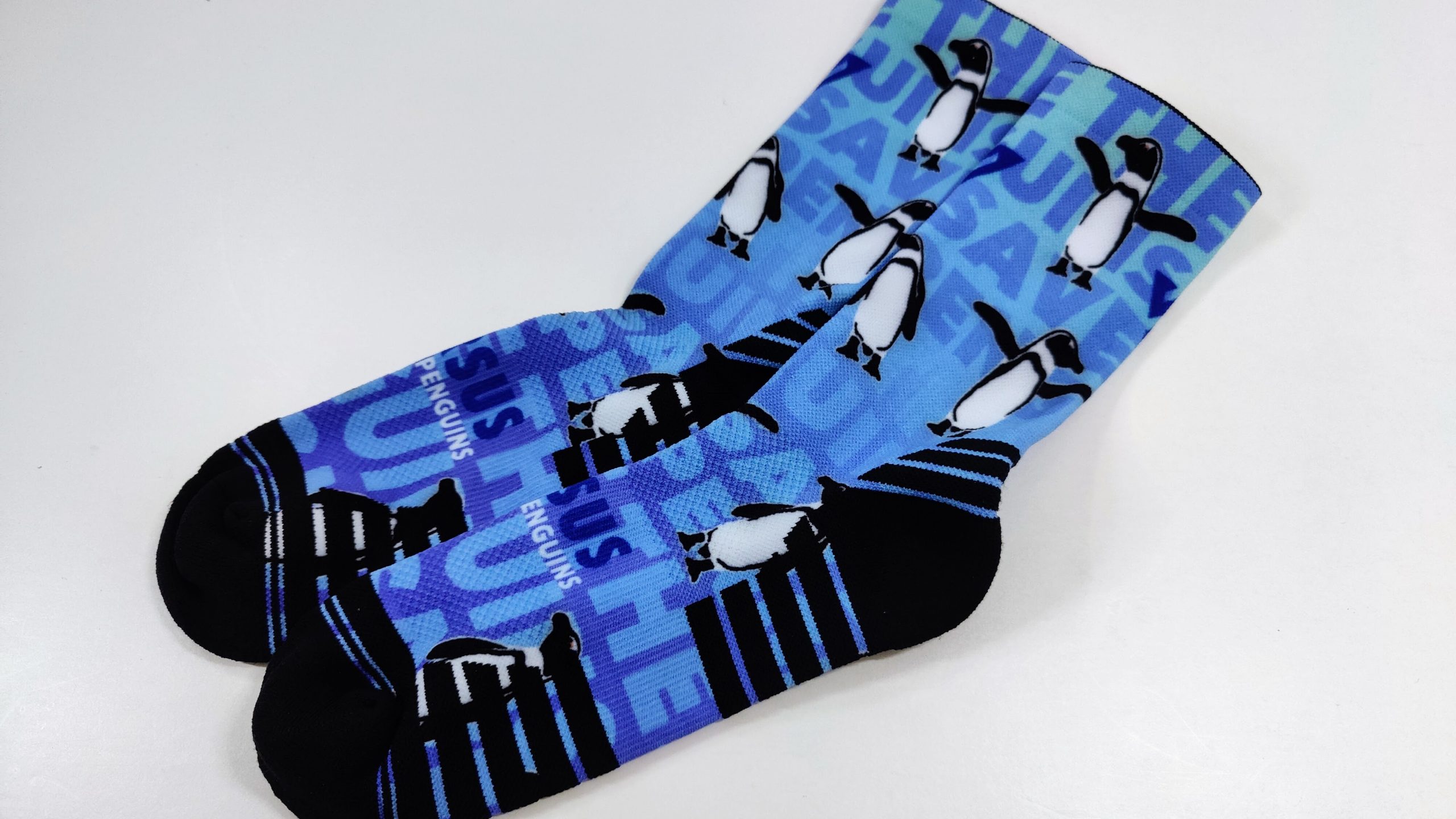 Blue sock with repeating black-and-white penguin illustrations on a lighter blue background, black toe and heel edge visible
