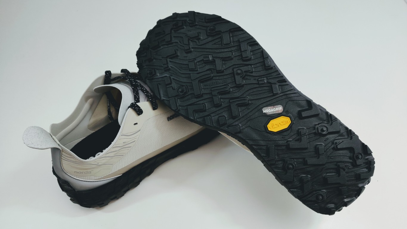 Gray and white hiking shoe with a chunky black treaded sole, shown from the side and bottom to display sole pattern (NordA brand).