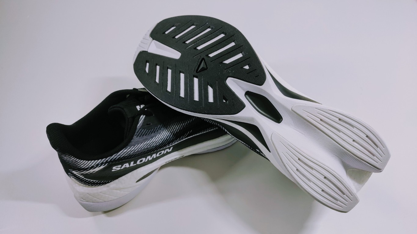 Pair of Salomon running shoes with black upper and white soles, soles facing the camera to show tread pattern.