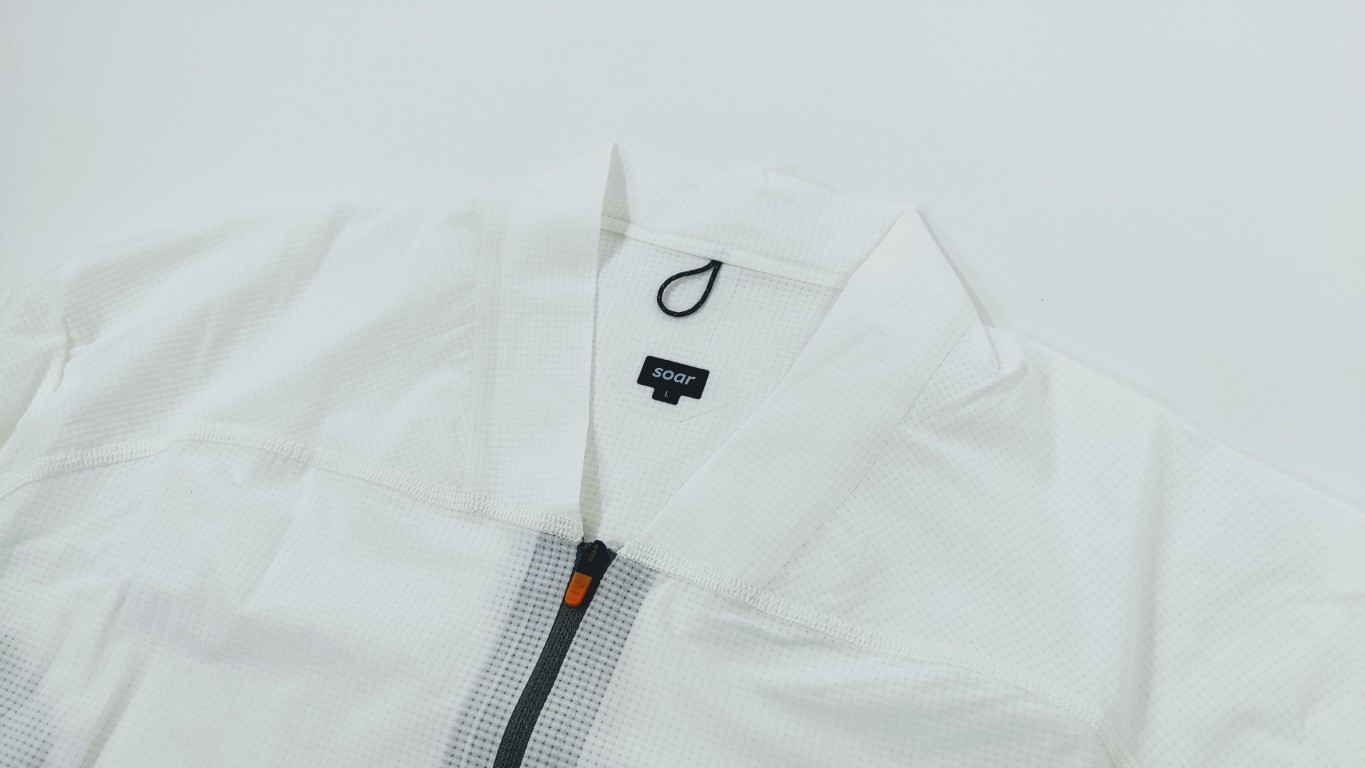 White zip-up jacket with textured fabric and a black zipper pull, laid flat to show front zipper and collar detail, brand tag visible behind the neck