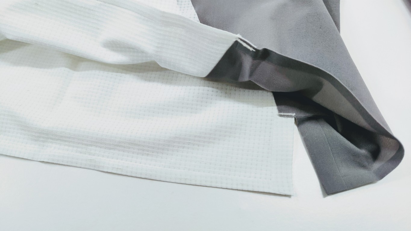 Close-up of white textured fabric overlapping with dark gray fabric on a light surface.