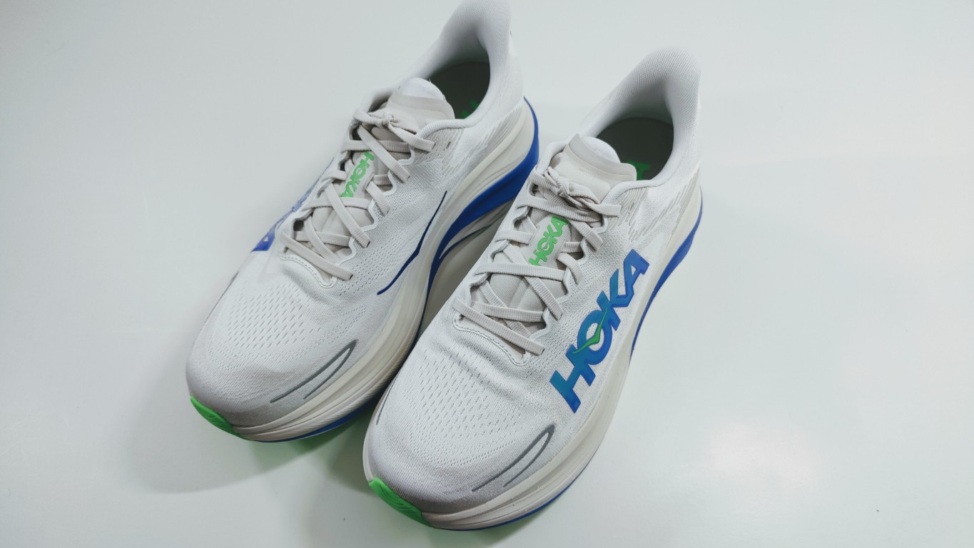 Pair of white Hoka running shoes with blue heel accents and lime green details on a light surface.