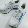 White HOKA running shoes with blue logo and green accents on a white surface, angled to show side and toe detail.