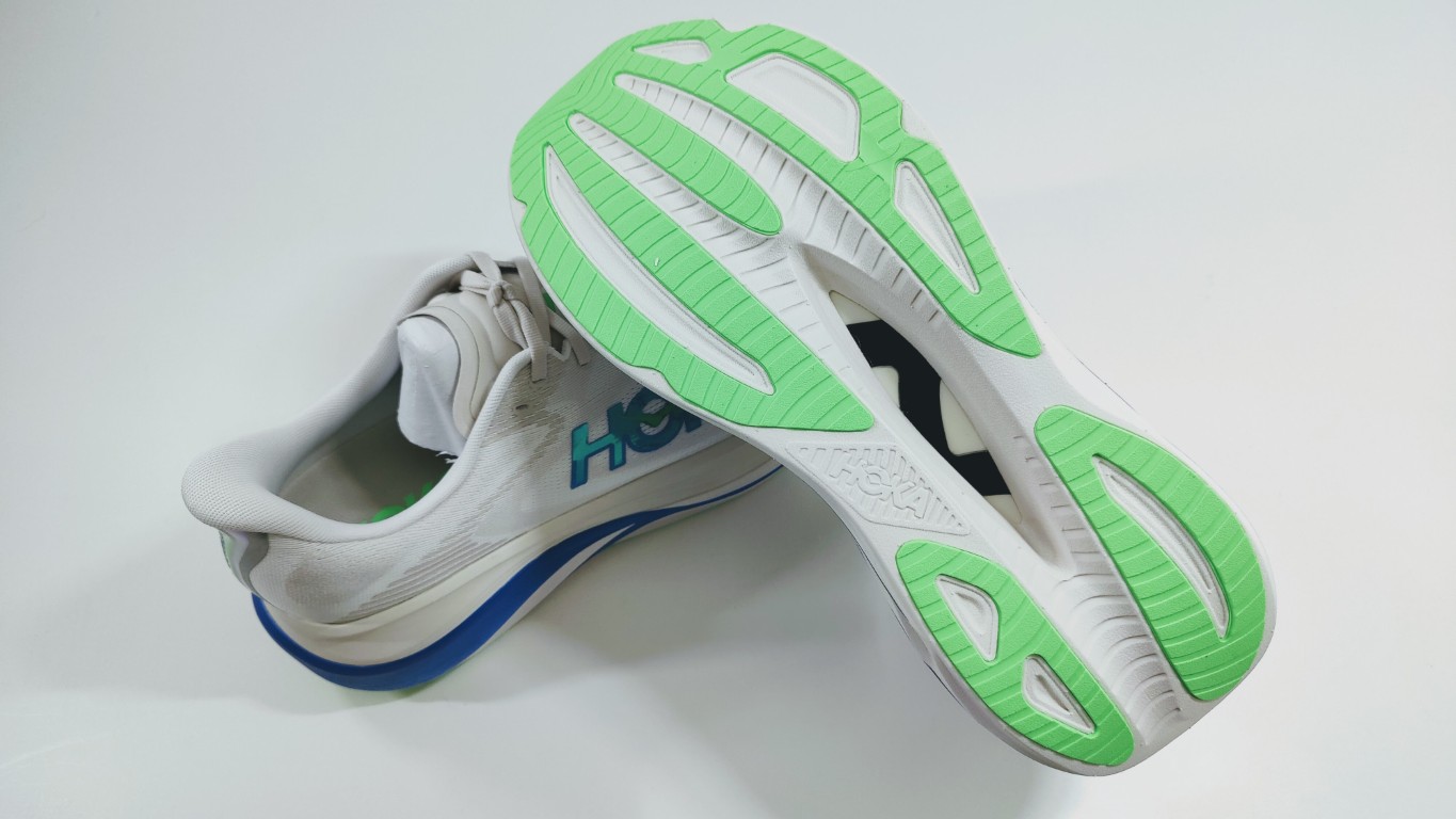 White running shoes with lime green outsole tread, placed on a white surface.