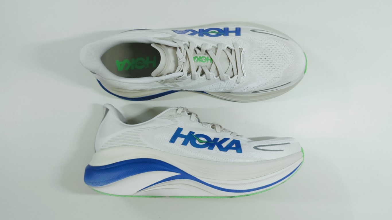 Top-down view of white Hoka running shoes with blue logo and green-accented soles.