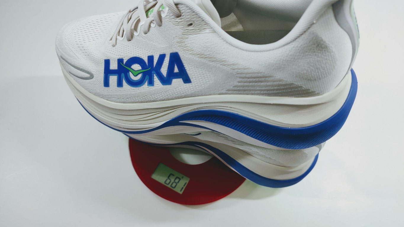Stack of white HOKA running shoes with blue soles resting on a red digital scale displaying 68.