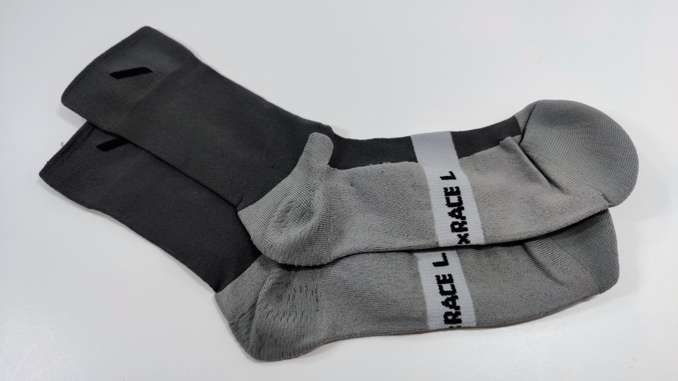 Pair of grey mid-calf running socks with dark grey cuffs and a 'RACE L' band across the foot, lying on a white surface.