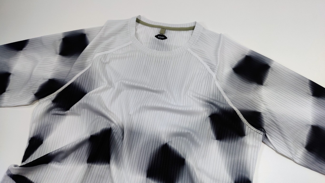 Close-up of a white textured running shirt with black blurred pattern and raglan seams at the shoulders, laid flat.
