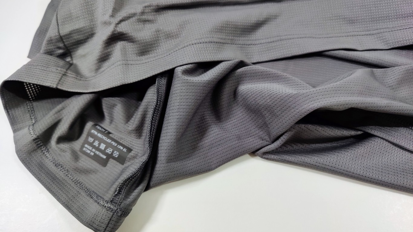 Close-up of grey mesh fabric with bonded seams and a black care label near the hem.