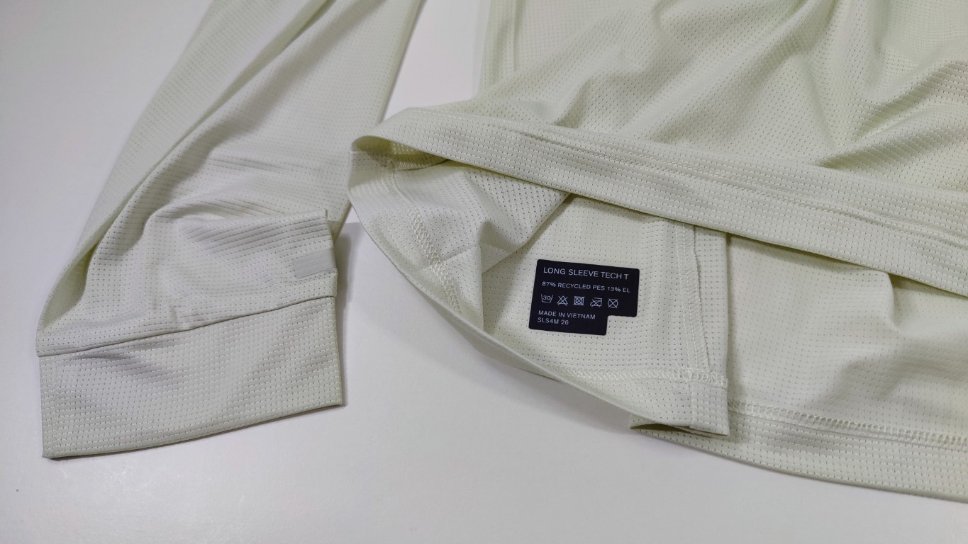 Close-up of the cuff and hem of a cream long-sleeve shirt with a black care label.