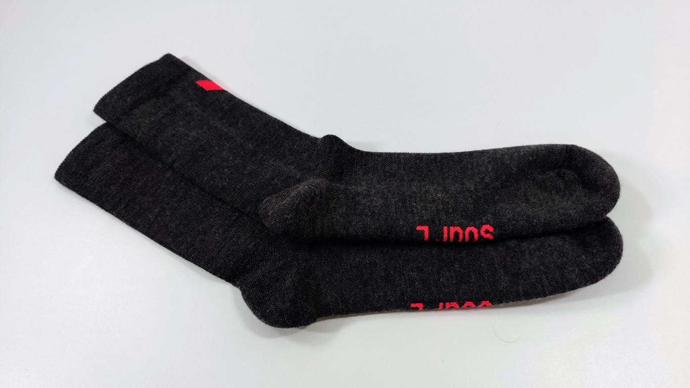 Pair of charcoal merino running socks with red lettering on the sole, lying on a white surface.