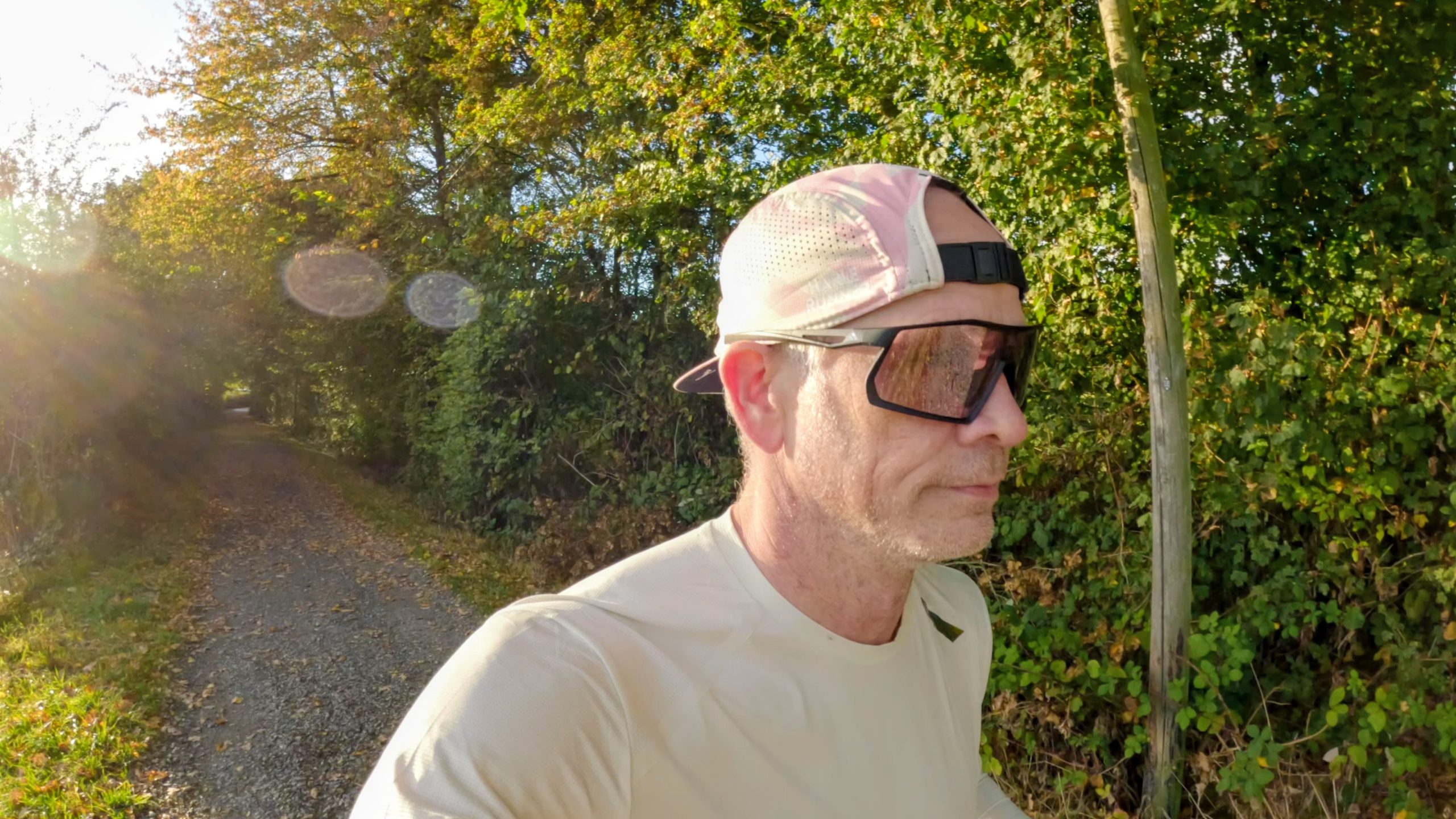 Runner wearing black sports sunglasses on a gravel path with low autumn sun shining through the trees