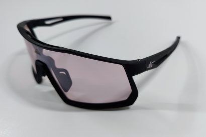 Black sports sunglasses with light violet shield lens seen from an angle on a white surface