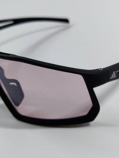 Black sports sunglasses with light violet shield lens seen from an angle on a white surface