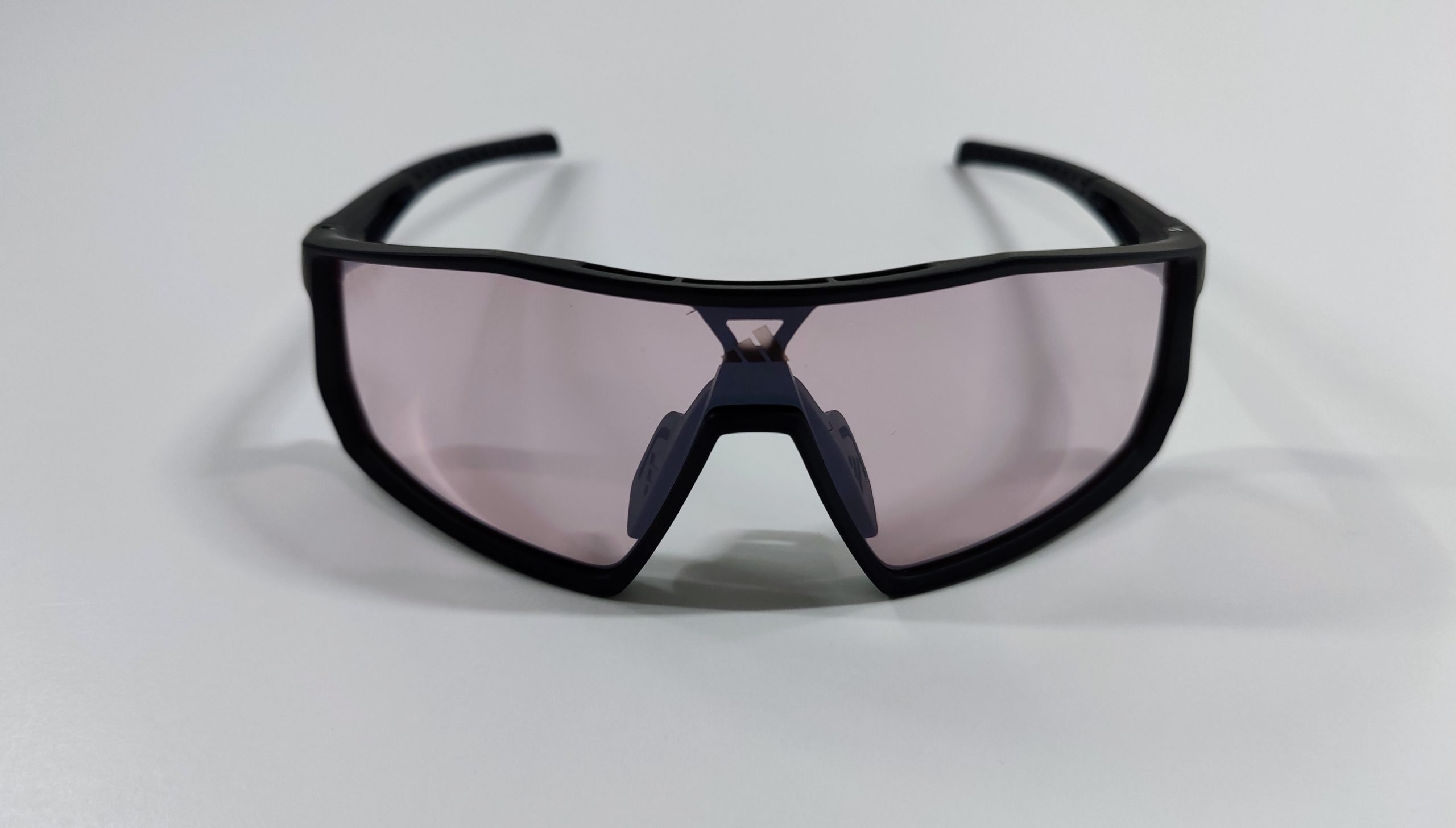 Front view of black shield sports sunglasses with light violet lens and nose pads on a white surface