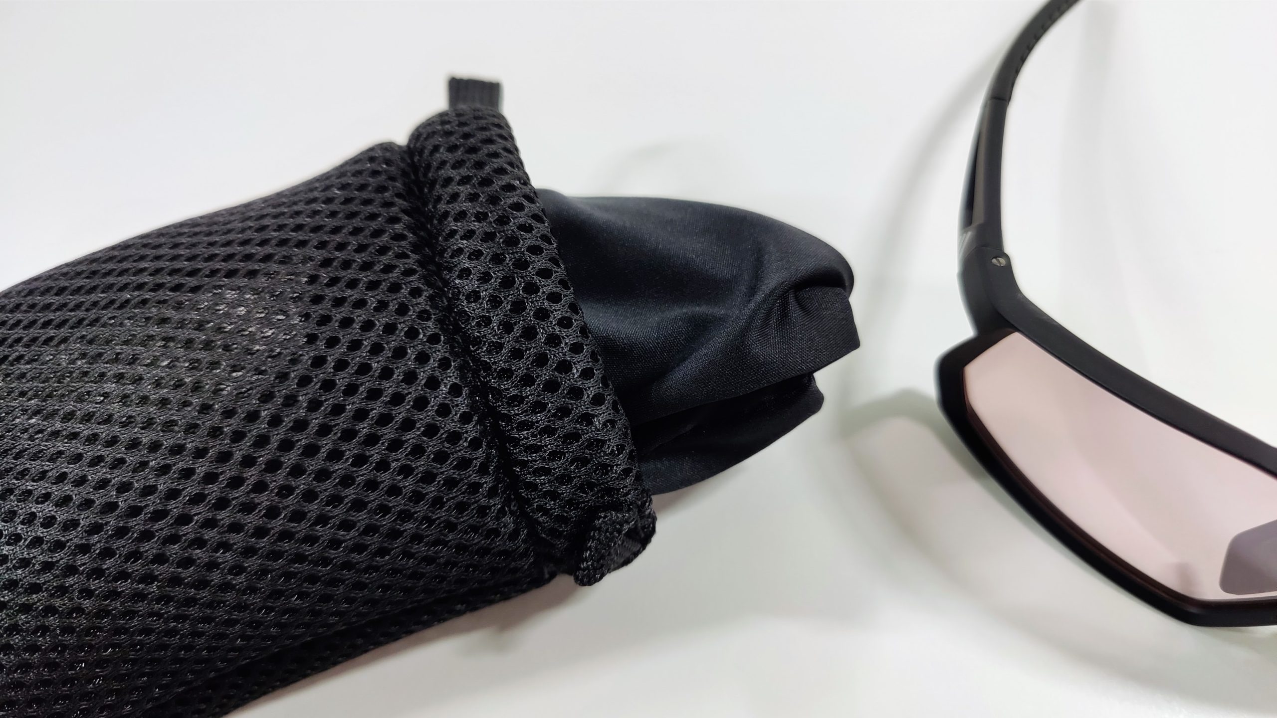 Black mesh pouch with a microfiber cleaning cloth next to the temple of black sports sunglasses on a white surface