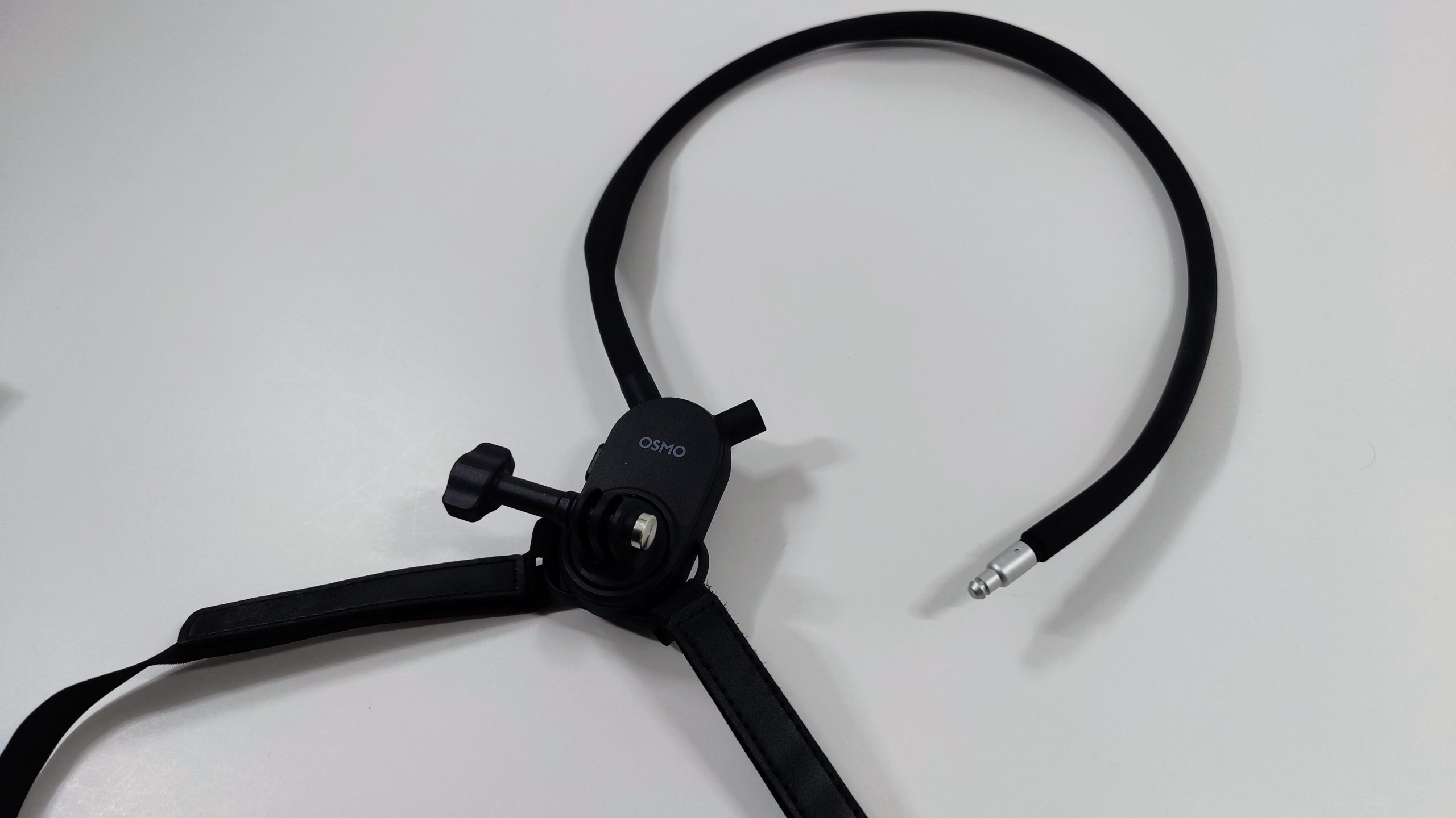 Black hanging neck mount with chest strap and quick-release plate on a white surface.