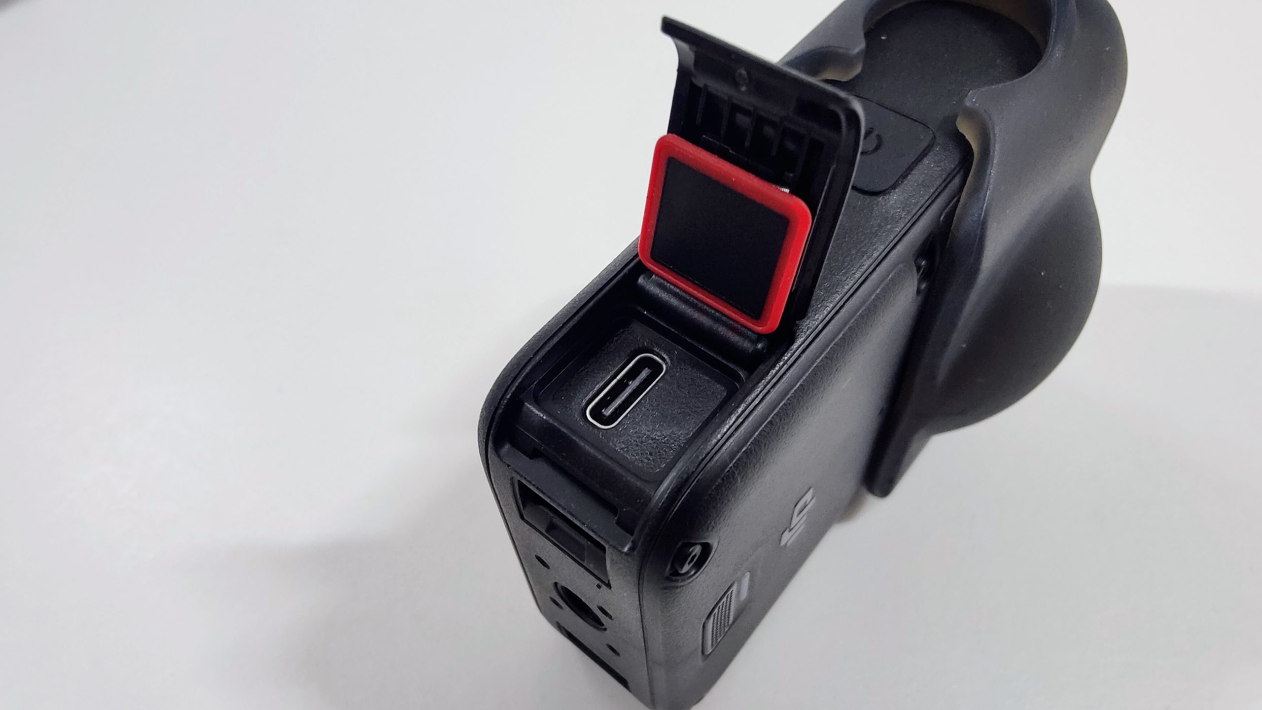 360 camera seen from above with the USB-C port flap open and a red seal cover.