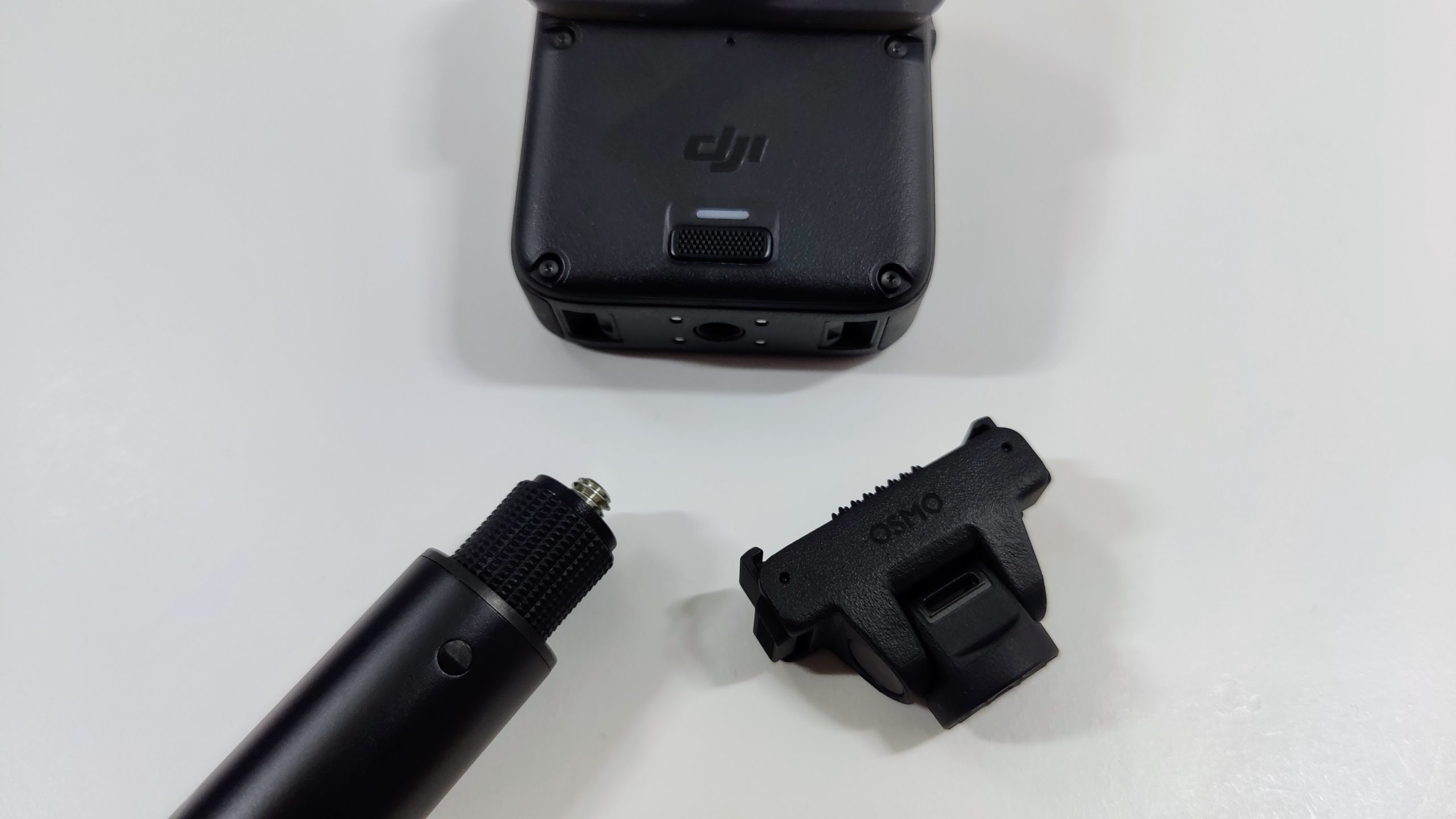 Selfie stick, folding adapter mount and 360 camera body separated on a white surface.