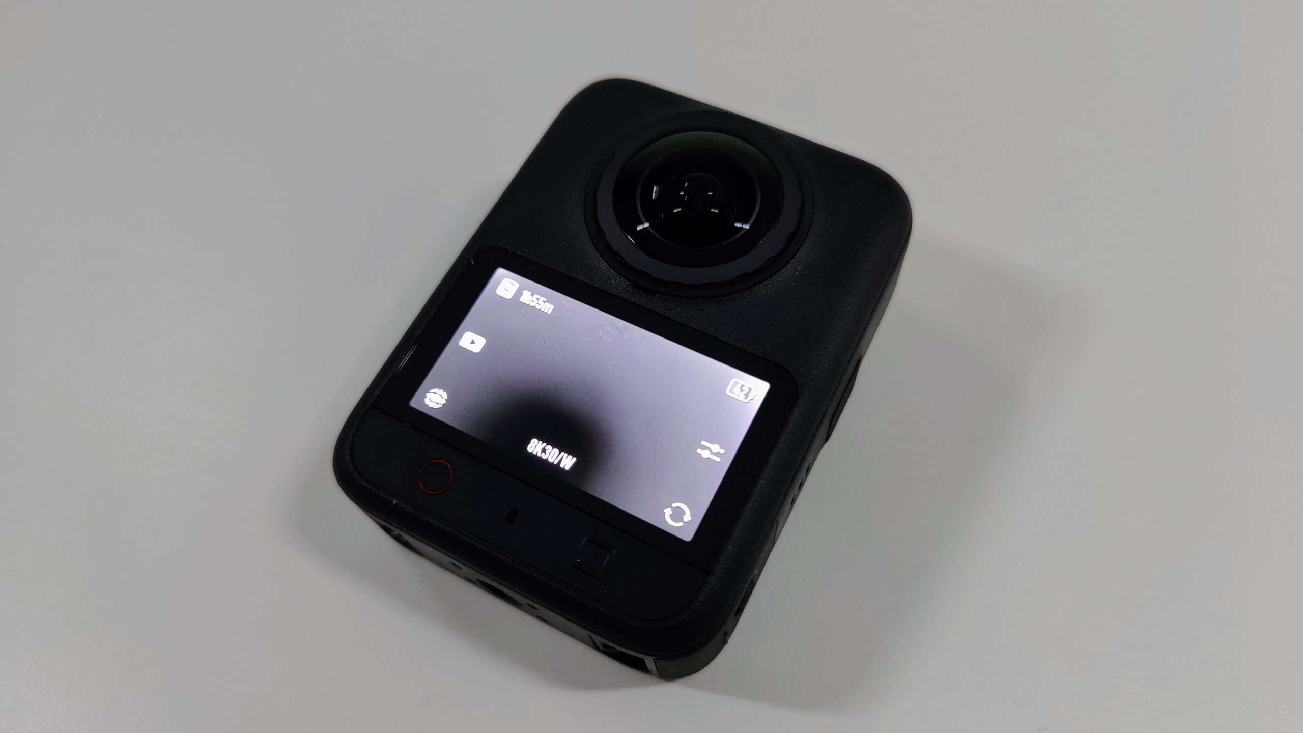 Front of the 360 camera showing the lens and a small touchscreen on a grey surface.