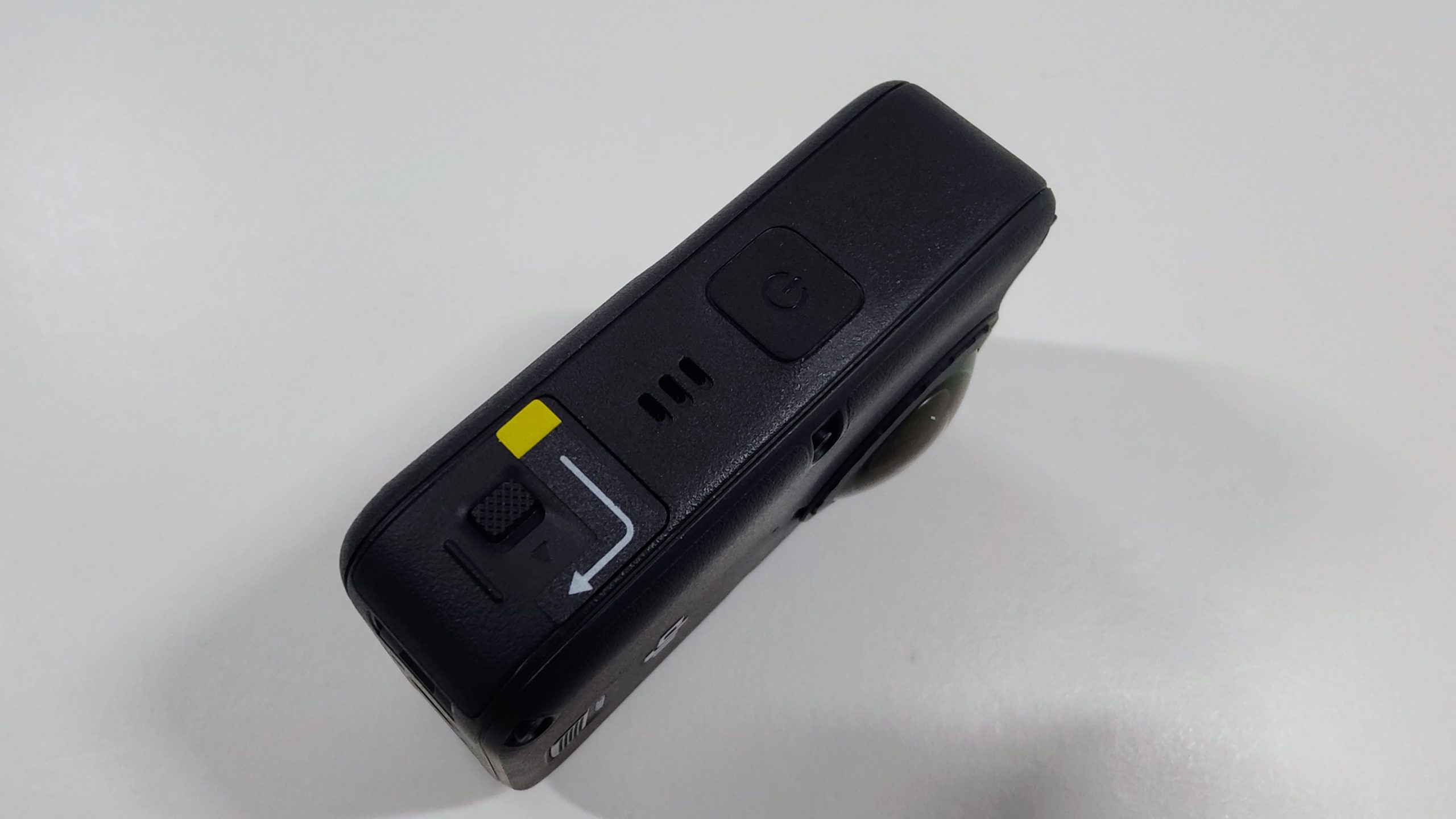 Camera side with button and microphone openings next to a yellow tab and quick-release slider.