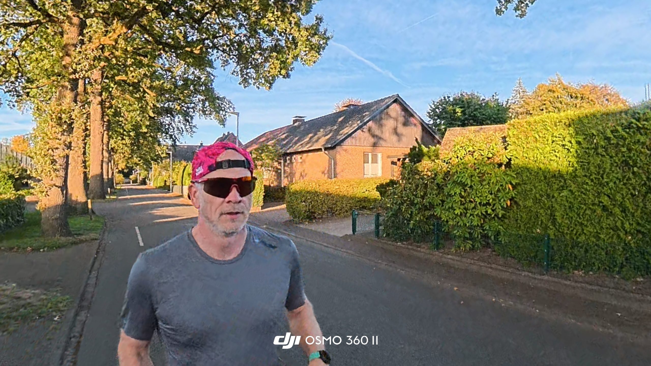 Selfie-perspective of a runner in a pink cap and sunglasses on a village road in the evening sun.