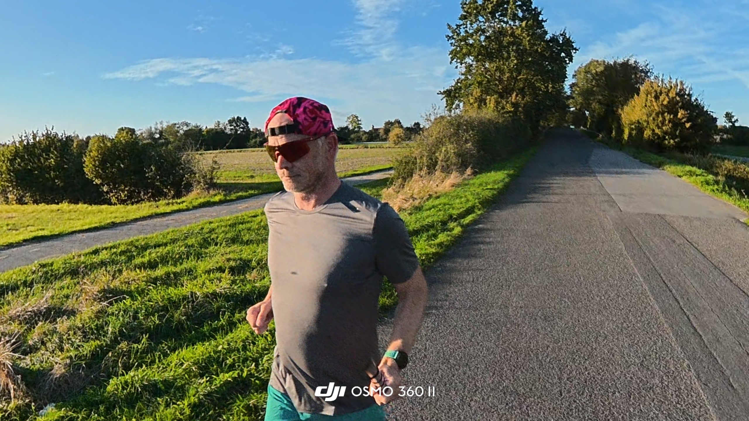 Runner on a country road next to green fields under a blue sky, shot from a low angle.