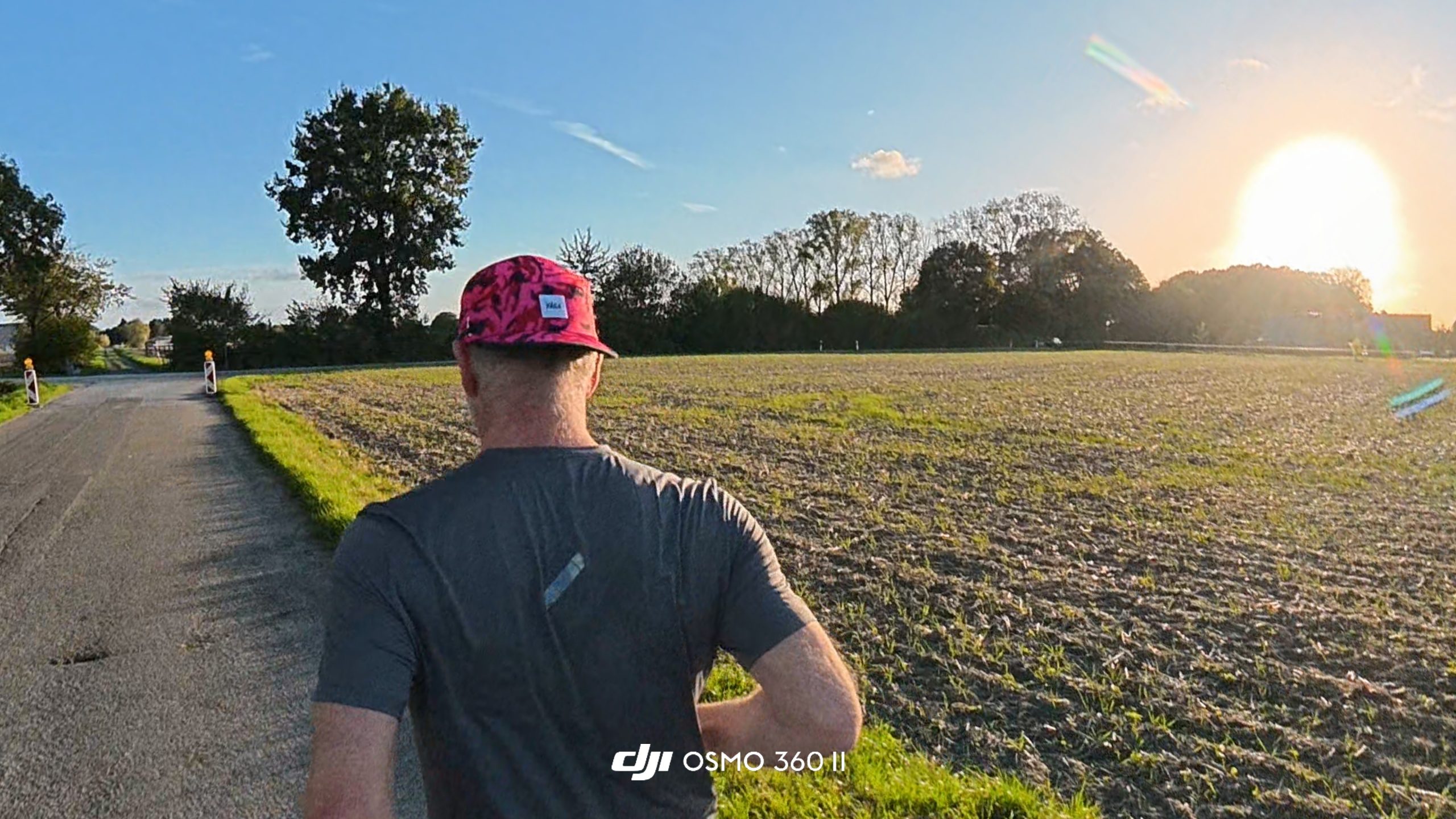 Runner seen from behind on a country road with a low sun over a ploughed field.