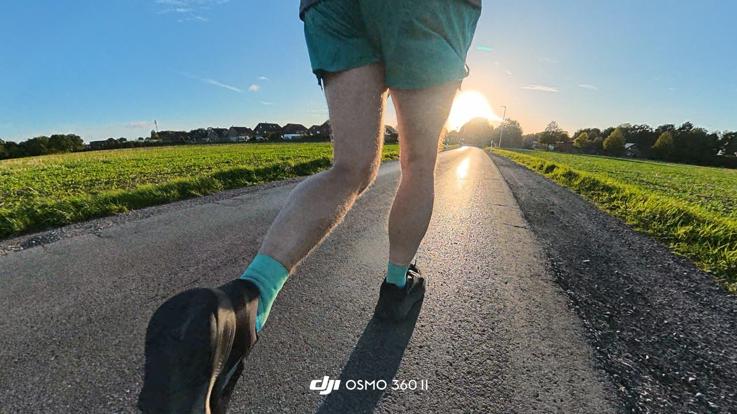 Low-angle view of a runner's legs and shoes on an asphalt road with the sun on the horizon.