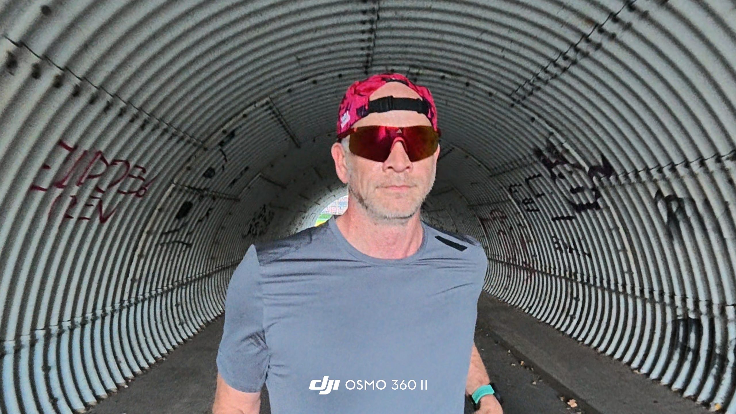 Runner in a corrugated metal tunnel with graffiti, filmed from the front.